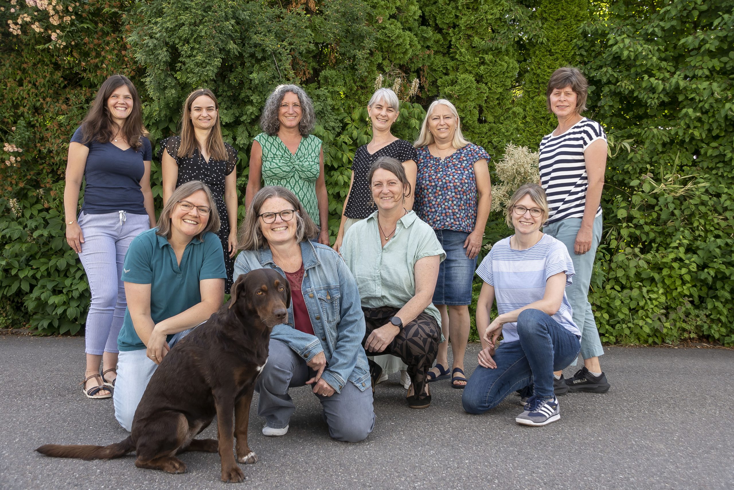 Team Kindertagespflege Landkreis Konstanz e.V. steht vor grüner Hecke, im Vordergrund Hund Lucy